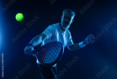 Padel player. Padel tennis open tour. Man athlete with paddle tenis racket and ball on blue background. Sport concept. Download a high quality photo for sports ads at social media stories or shorts. photo