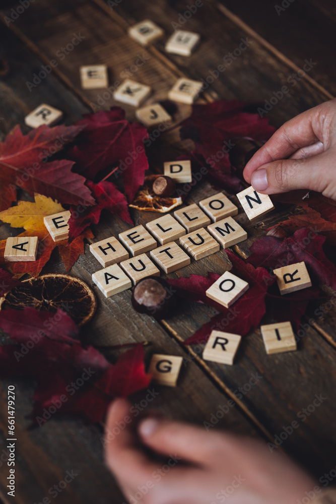 Obraz premium Woman's hands with Hello autumn text on dark wooden background. Composition with bright autumn leaves, pumpkin, dry citrus, walnut. Cozy fall mood concept. Flat lay, close up, top view, macro