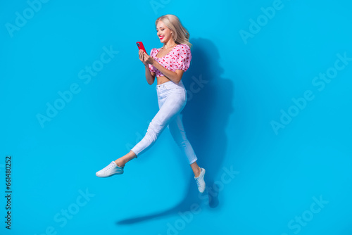 Fototapeta Naklejka Na Ścianę i Meble -  Full size photo of pretty young girl running hold telephone dressed stylish pink cherry print clothes isolated on blue color background