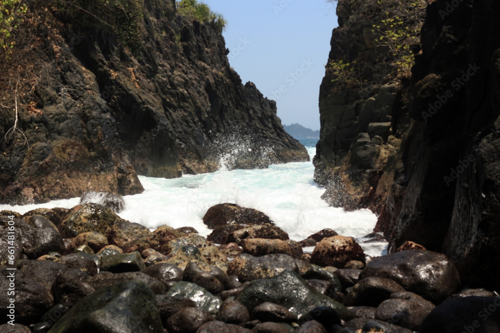 Obraz premium Waves splashing against rocks and pebblesin the seashore. Bright sunny day in the rocky beach.