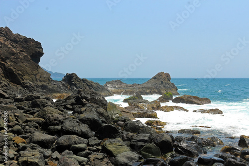 Waves splashing against rocks in the seashore. Bright sunny day in the rocky beach.