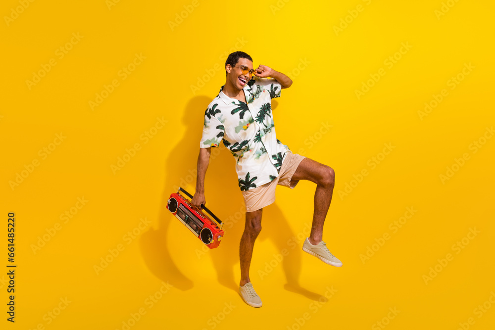 Full size photo of handsome young guy dancing have fun boom box dressed stylish palms print outfit isolated on yellow color background