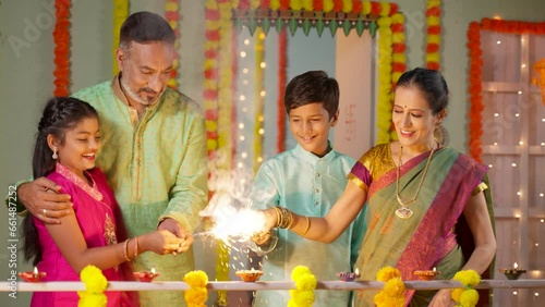 Happy Grandparents playing with sparklers or Crackers with Kids near balcony at home during diwali festival celebration - concept of Traditional culture, Familt generation and Caring family
