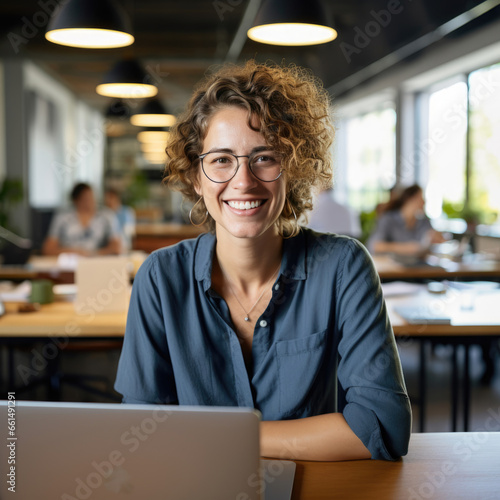Casual shot of a smiling businesswoman behind her laptop at her working desk looking at the camera, daylight