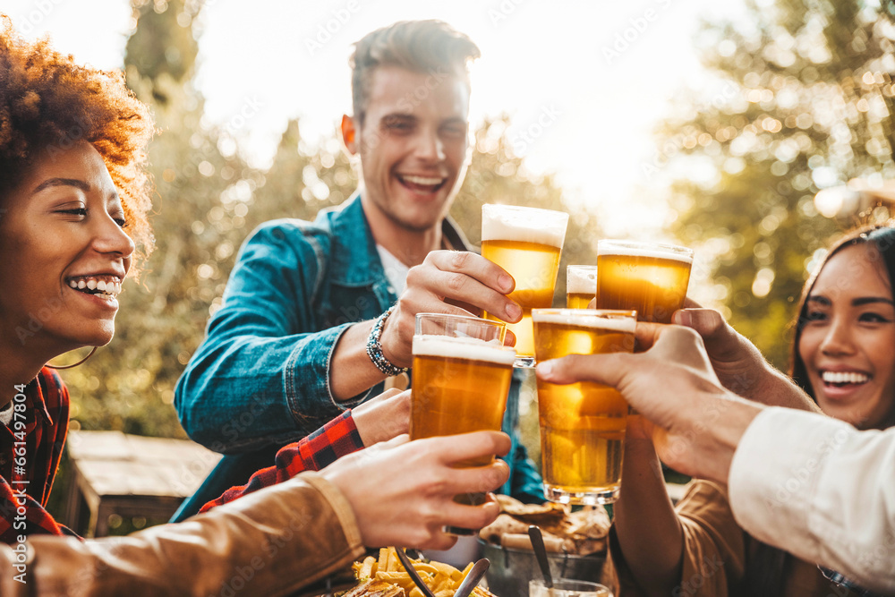 Group of multi ethnic friends having backyard dinner party together - Diverse young people sitting at bar table toasting beer glasses in brewery pub garden - Happy hour, lunch break and youth concept - obrazy, fototapety, plakaty 