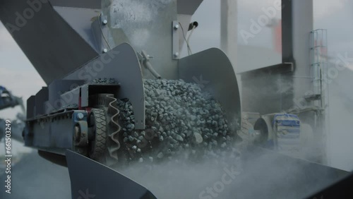 Rotating pulleys loads gravel grains in container at mining quarry. Conveyor carries stone building materials with dust clouds at plant