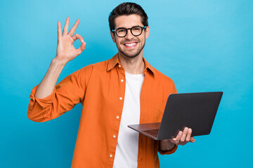 Photo of positive handsome guy hold netbook demonstrate okey symbol eshopping isolated on blue color background