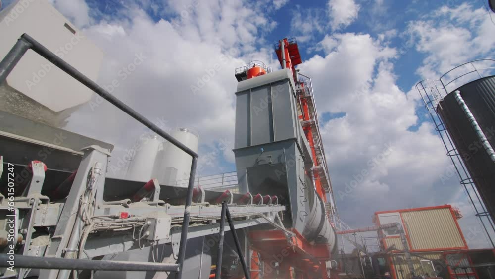 Outside conveyor transports materials to production tower at asphalt plant. Road pavement mix manufacturing facilities against white clouds Outside conveyor transports materials to production tower at asphalt plant. Road pavement mix manufacturing facilities against white clouds