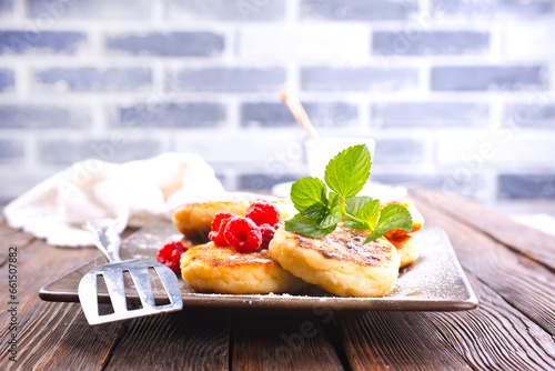 Traditional sweet syrniki or cottage cheese pancakes served with sweet cream and fresh raspberries in a white plate over table. photo