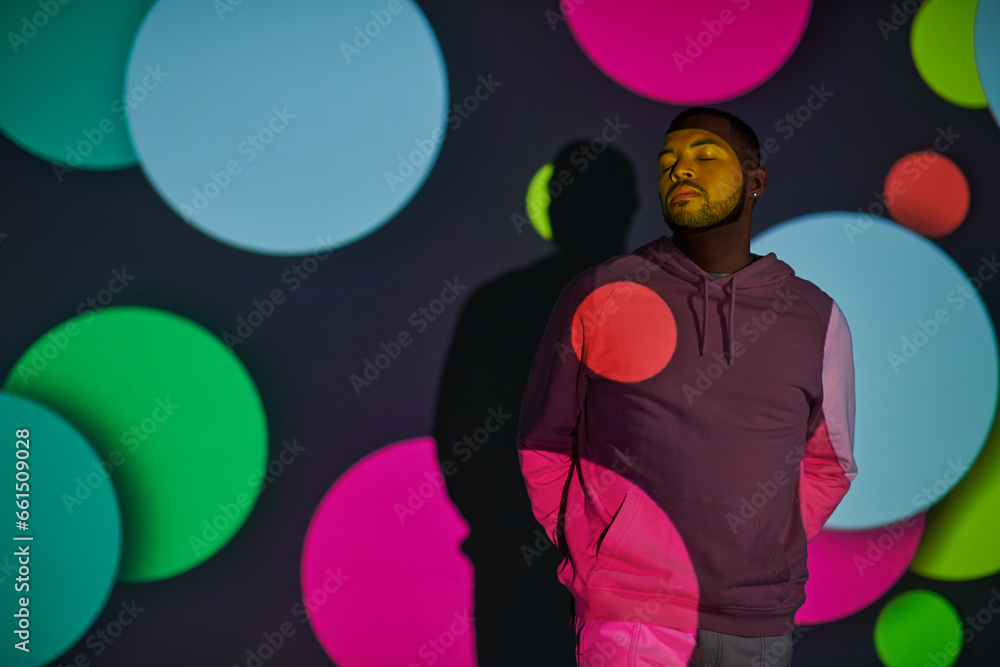 handsome man with hands behind back and closed eyes in digital projector lights, fashion concept