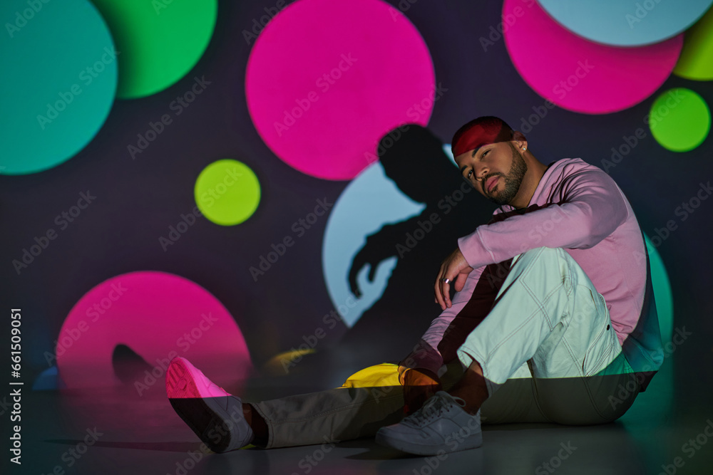 handsome young man sitting on floor slightly smiling in digital projector lights, fashion concept handsome young man sitting on floor slightly smiling in digital projector lights, fashion concept