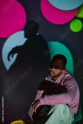 good looking man in pink hoodie sitting on floor in digital projector lights, fashion concept