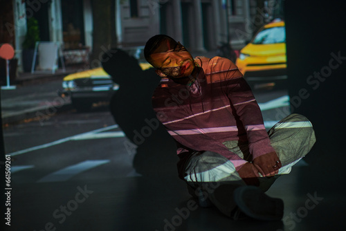 young african american man reclining slightly on floor with hands on crossed legs, fashion concept