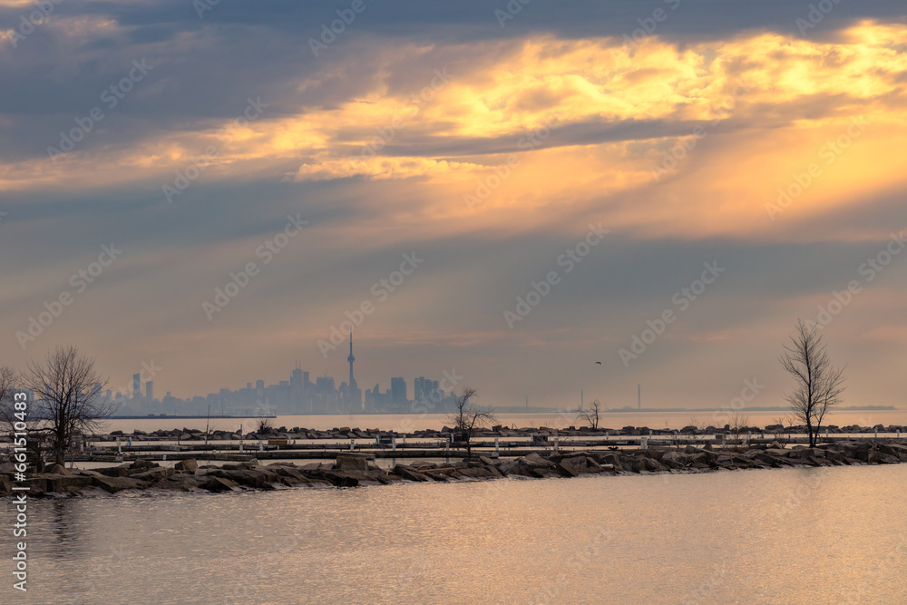 Dramatic moody sunrise light with sun rays over Lake Ontatio with the Toronto skyline in the background. Port Credit, Mississauga - obrazy, fototapety, plakaty 