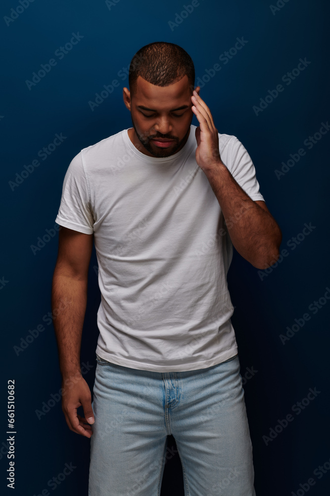 young man in stylish attire posing on dark blue backdrop with hand near forehead, fashion concept young man in stylish attire posing on dark blue backdrop with hand near forehead, fashion concept