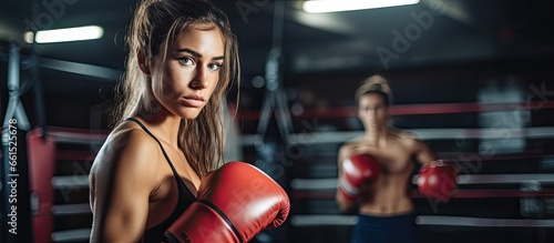 Young woman in boxing ring trains with partner and sparring equipment nearby