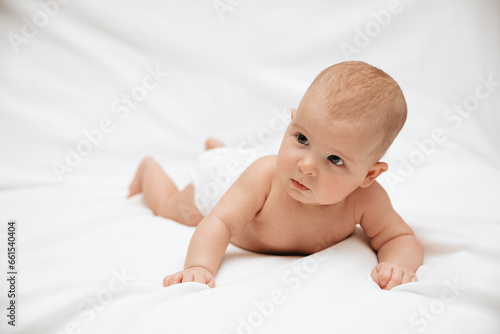 Bild auf Leinwand Little newborn baby in a diaper is trying to crawl on a white blanket