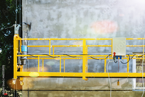 Suspended motor scaffolding platform on facade of residential building under renovation. High-altitude works, residential building facade plastering.