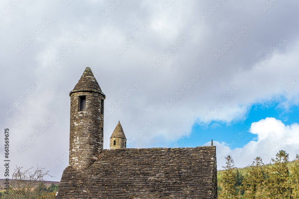 Old brick building with round tower in sunshine at churchyard in Glendalough's monastic town. Early medieval monastic settlement founded by St Kevin in the 6th century