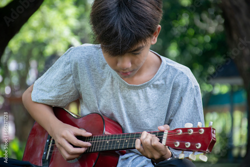Asian cute boy playing guitar in the front yard of his own house happily, soft focus, concept for recreational activity and free times hobbies of children around the world.