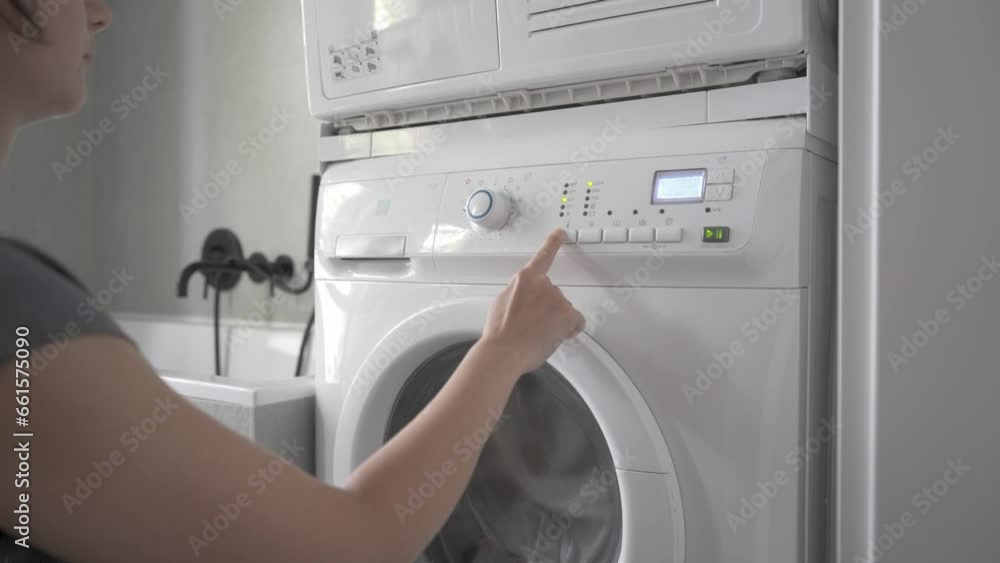 The woman turns on the home washing machine, selects a cycle for washing clothes and starts washing The woman turns on the home washing machine, selects a cycle for washing clothes and starts washing
