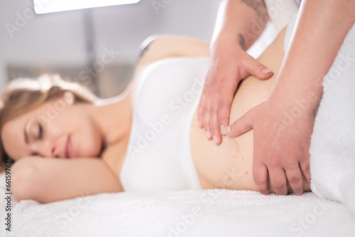 Crop masseuse touching belly of female client