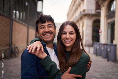 Portrait of young multiracial couple embracing happy smiling face on street. Friends cheerful hugging people positive expression looking at camera. Nice loving partner posing for photo outdoor.