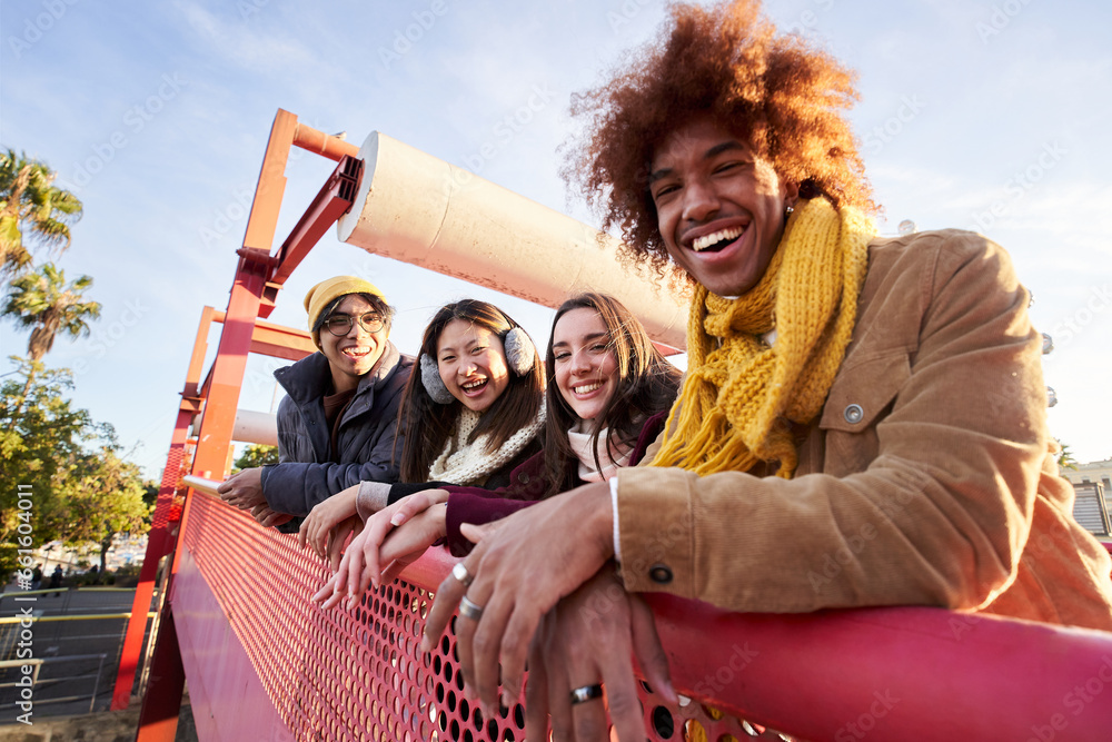 Multi-ethnic group smiling friends gathered on street leaning on railing. Happy young people enjoying together outdoors pose for portrait. Social relationships in college students of Generation z. - obrazy, fototapety, plakaty 