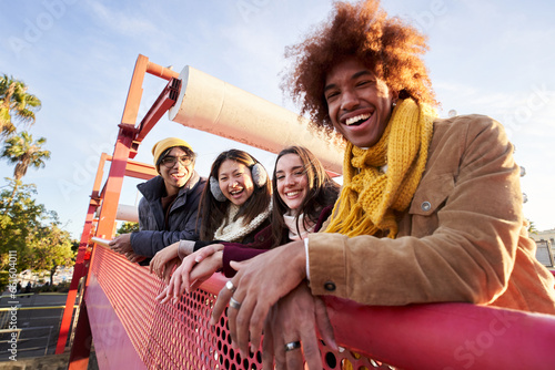 Multi-ethnic group smiling friends gathered on street leaning on railing. Happy young people enjoying together outdoors pose for portrait. Social relationships in college students of Generation z.
