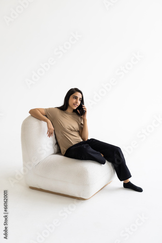 Happy young Indian woman talking on mobile phone, looking away, standing by white background.