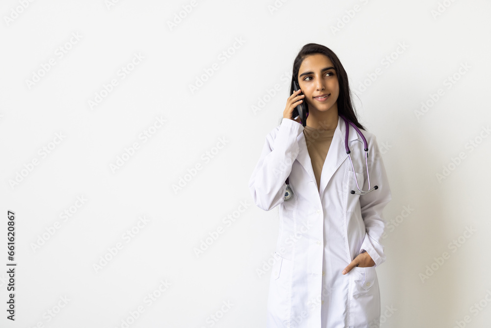 Indian female doctor talking mobile phone in white coat and red stethoscope in white background. Indian female doctor talking mobile phone in white coat and red stethoscope in white background.