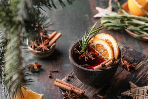 Mulled wine in ceramic mug with orange slices and spices. Christmas hot drink on wooden table with xmas tree branches, festive card text space