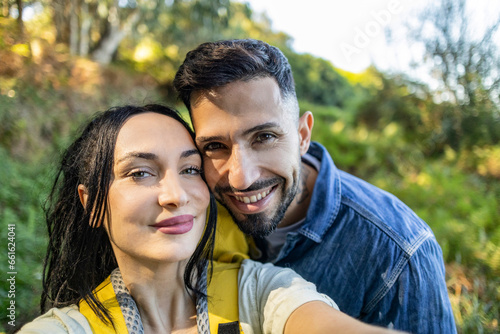 A happy Caucasian couple is taking a selfie smiling at the camera in front of the mountain while hiking in Europe. traveling backpackers.