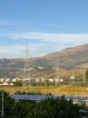 Overhead line pylons, high voltage pylons in meadow with mountains on background
