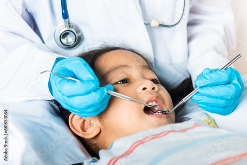 Dental kid health examination. Doctor examines oral cavity of little child uses mouth mirror to checking teeth cavity, Asian dentist making examination procedure for smiling cute little girl