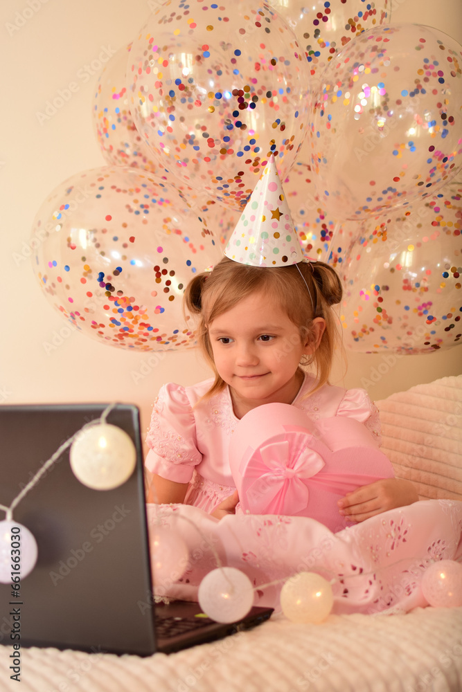 Fototapeta premium Birthday online. Child celebrates birthday by laptop. A little girl celebrates her birthday with her parents, relatives and friends via video call. Holiday in isolation. Little princess
