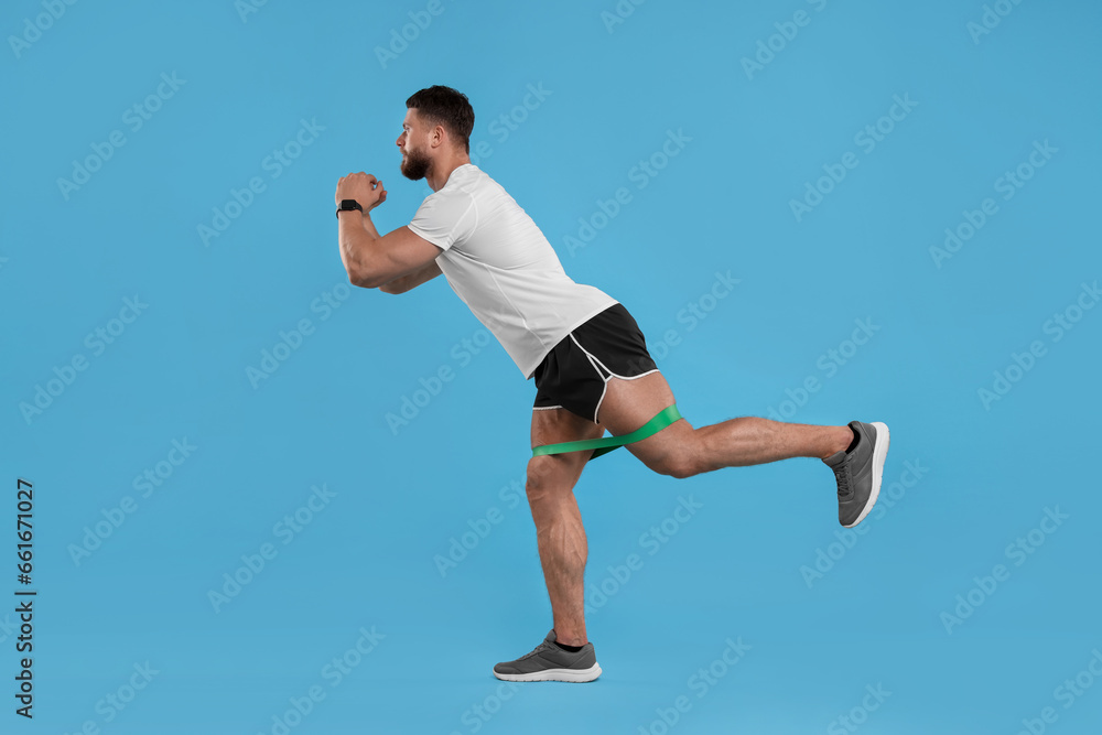 Fototapeta premium Young man exercising with elastic resistance band on light blue background