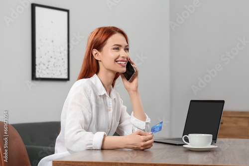Happy woman with credit card using smartphone for online shopping at wooden table in room. Space for text