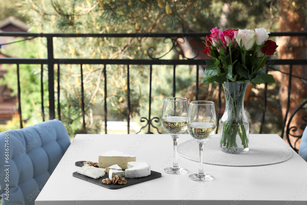 Beautiful roses, glasses of wine and snacks on white table at balcony