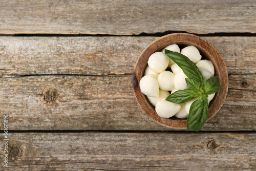 Tasty mozzarella balls and basil leaves in bowl on wooden table, top view. Space for text