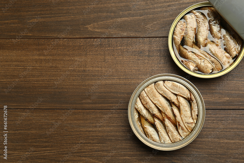 Open tin cans of sprats on wooden table, flat lay. Space for text Open tin cans of sprats on wooden table, flat lay. Space for text