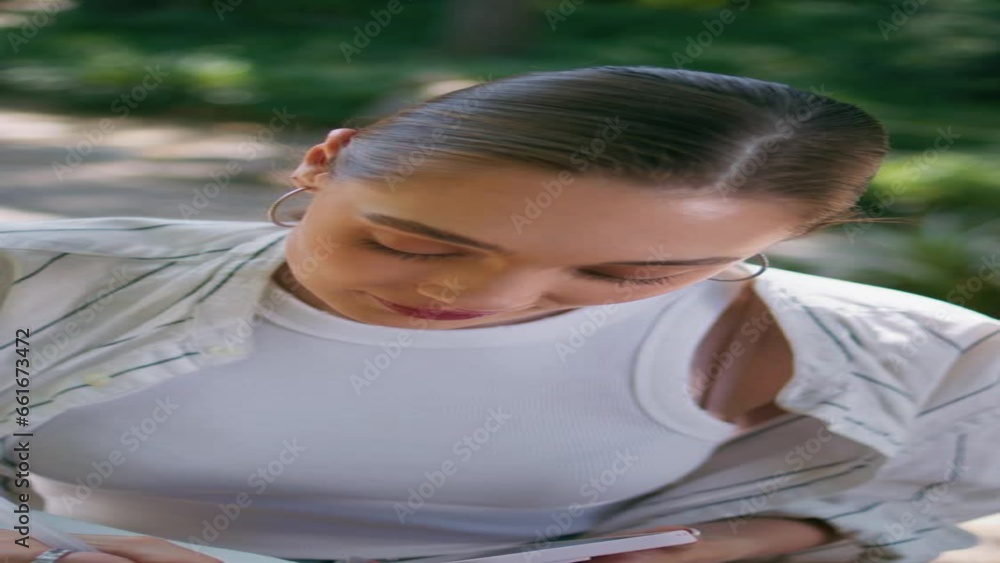 Beautiful woman creating text to notepad in park with mobile close up vertically Beautiful woman creating text to notepad in park with mobile close up vertically