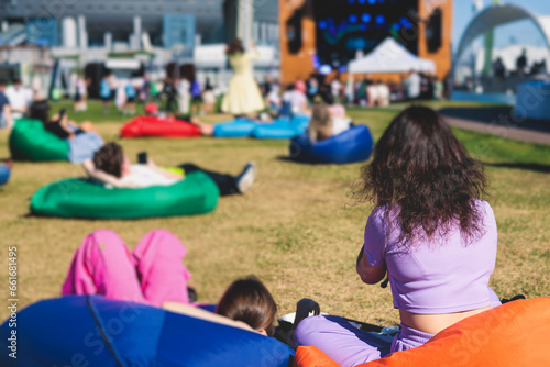 Crowded open air festival concert with musicians band on stage, rock show performance, with concert-goers attendees on beanbags, audience sitting on bean bag chair on a grass lawn on summer festival © tsuguliev