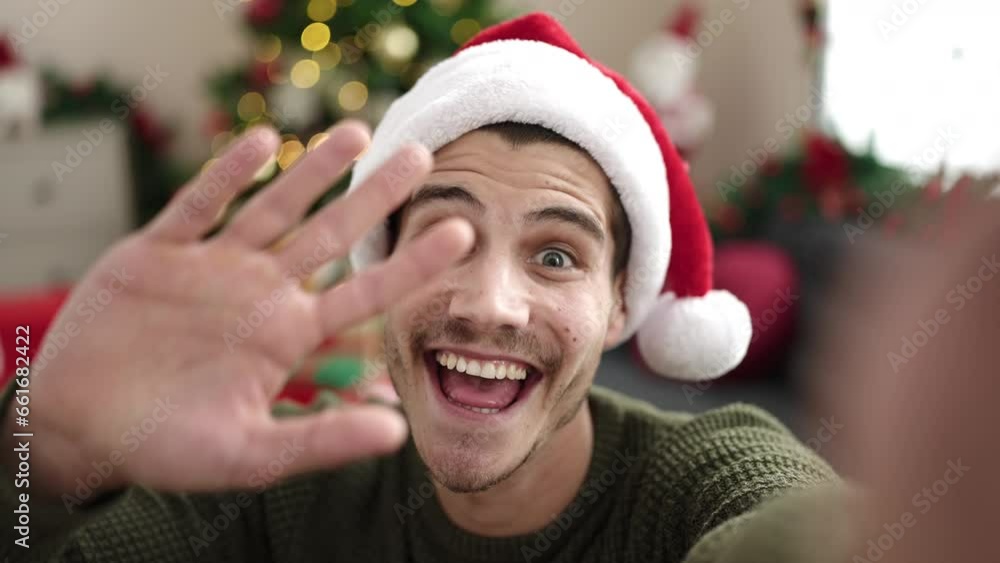 Young hispanic man having video call sitting on sofa by christmas tree at home Young hispanic man having video call sitting on sofa by christmas tree at home