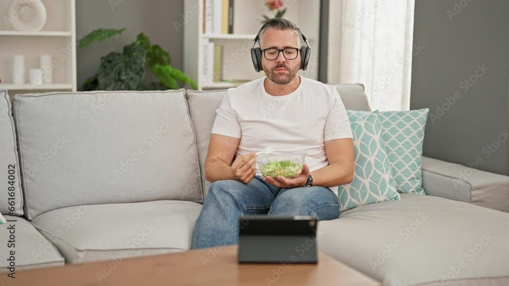 Grey-haired man eating salad watching video on touchpad at home Grey-haired man eating salad watching video on touchpad at home