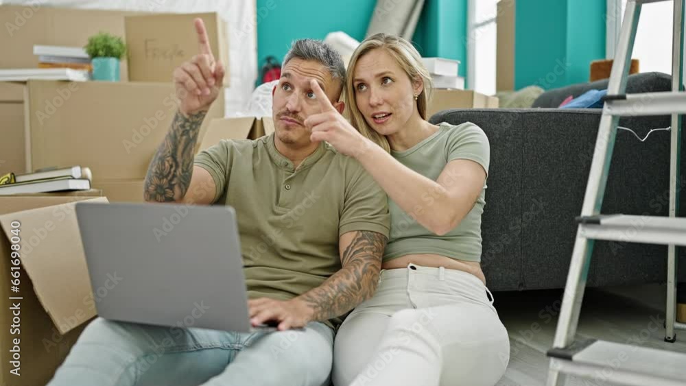 Man and woman couple using laptop looking around at new home Man and woman couple using laptop looking around at new home