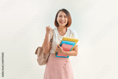 Portrait of smiling woman holding book and backpack leaning on white background