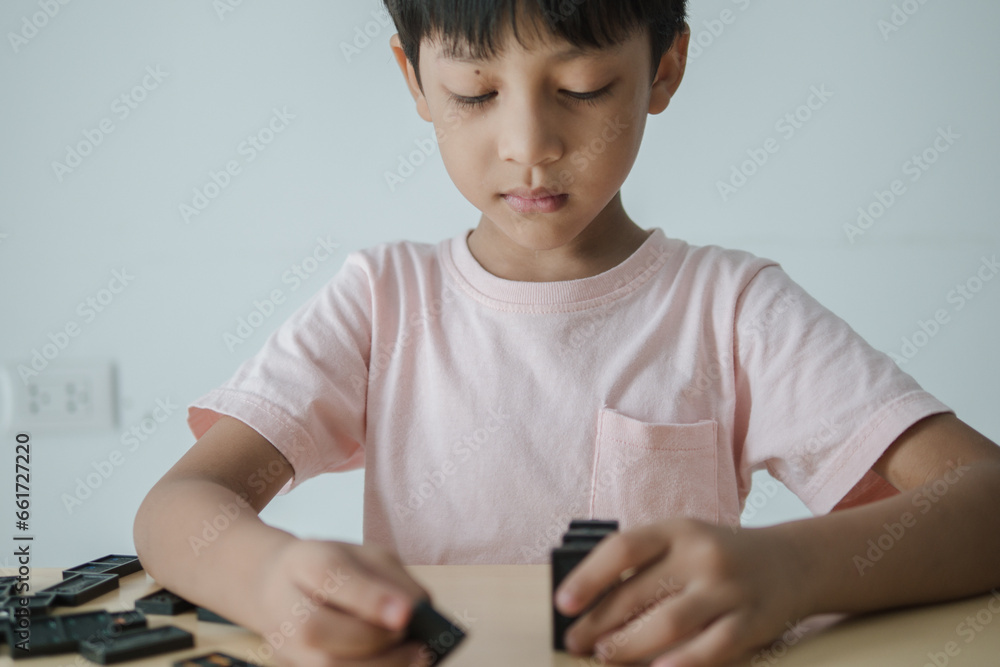 Cute Asian Thailand boy, 3-6 years old, standing playing dominoes on a wooden table inside the house, learning in the house, with copy space.