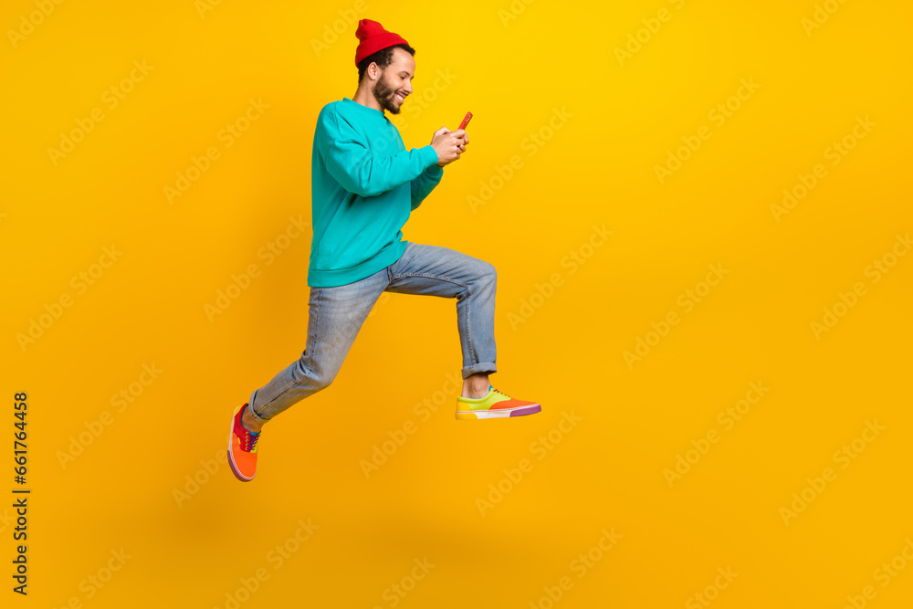 Full length photo of cheerful man wear turquoise pullover running to empty space look at smartphone isolated on yellow color background Full length photo of cheerful man wear turquoise pullover running to empty space look at smartphone isolated on yellow color background