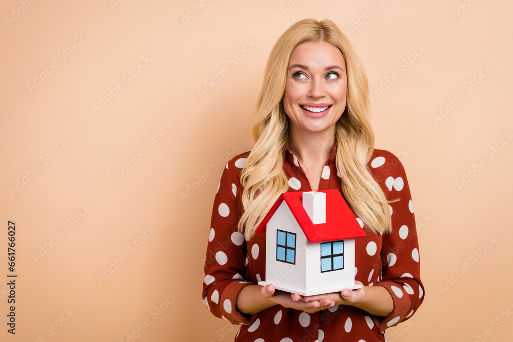 Portrait of gorgeous nice lady toothy smile hands hold small house look empty space isolated on beige color background Portrait of gorgeous nice lady toothy smile hands hold small house look empty space isolated on beige color background